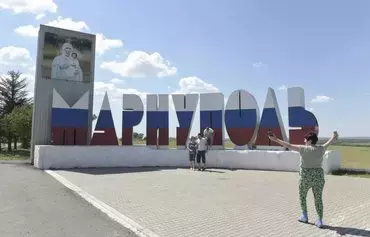 People pose for a photograph in front of a sign giving the name of Mariupol in Russian and painted in the colors of the Russian flag, in Mariupol, Ukraine, on August 16. [AFP]