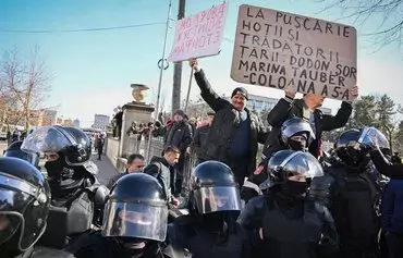 Supporters of Moldovan President Maia Sandu hold placards including one reading 'Thieves and traitors to jail, [former president Igor] Dodon, Șor, Marina Tauber to jail' with Moldovan police in riot gear in the foreground, amid a protest organized by Tauber, a Moldovan member of parliament, on behalf of the Șor opposition party in Chisinau on March 12. [Daniel Mihailescu/AFP]