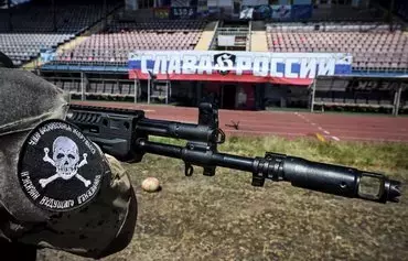 A volunteer of the Espanola special force unit, a detachment of Russian football hooligans, guards the football stadium in Mariupol last June 22 in front of a banner reading 'Glory to Russia!' [Alexander Nemenov/AFP]