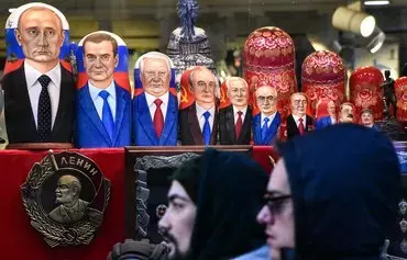 People walk past traditional Russian matryoshka dolls -- bearing Russian and Soviet leaders (from left) Vladimir Putin, Dmitry Medvedev, Boris Yeltsin, Mikhail Gorbachev, Konstantin Chernenko, Yuri Andropov, Leonid Brezhnev, Nikita Khrushchev, Joseph Stalin and Vladimir Lenin -- displayed in a gift shop in Moscow on December 16, 2018. [Vasily Maximov/AFP]