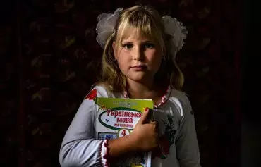 Antonina, 9, at home in Pokrovske village, Ukraine, holds a Ukrainian language schoolbook after an online lesson on her first day of class on September 1, 2022, amid the Russian invasion of her country. [Dimitar Dilkoff/AFP]