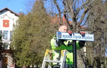 A worker in Vilnius, Lithuania, installs a Ukrainian-language sign reading 'Ukrainian Heroes' Street' on a formerly nameless road leading straight to the Russian embassy (seen in the background), on March 9, 2022. [Petras Malukas/AFP]