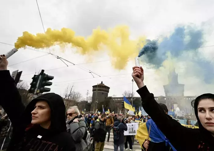 Protesters hold blue and yellow smoke grenades during a demonstration to protest against the invasion of Ukraine by Russia, on February 24, in Milan, Italy. [Gabriel Bouys/AFP]