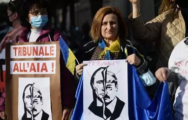 A woman holds an Italian-language placard reading 'International Criminal Court in The Hague' above the portraits of both Russian President Vladimir Putin and Belarusian leader Alyaksandr Lukashenka during a demonstration in support of Ukraine in front of Russia's embassy in Rome on February 24, 2022. [Filippo Monteforte/AFP]