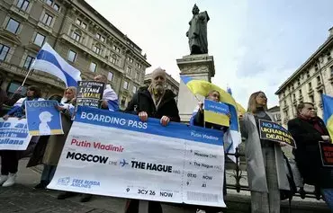 A man holds a giant mock boarding pass marked 'Moscow - The Hague' with the name of Vladimir Putin during a protest against the Russian president, on February 24, in Milan. [Gabriel Bouys/AFP]