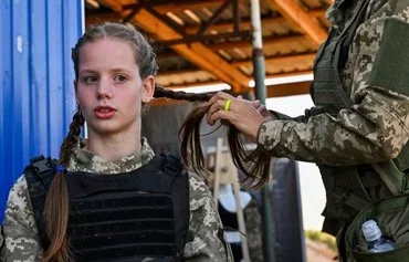 A female Ukrainian cadet, wearing a new military uniform designed specially for women, has her hair braided as she takes part in training during an event called 'The uniform matters,' which the army organized to present the outfit and test it under military training conditions, on the outskirts of Kyiv on July 12. [Sergei Supinsky/AFP] [Sergei Supinsky/AFP]