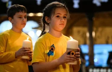 Children hold candles at the start of the ecumenical prayer service at Ukrainian Catholic Cathedral in London on February 24, 2023, marking the first anniversary of Russia's invasion of Ukraine. [Daniel Leal/AFP]