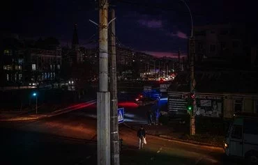 A pedestrian crosses a street at night in Mykolaiv, Ukraine, as the city undergoes a power outage on December 29, 2022, amid the Russian invasion of Ukraine. [Dimitar Dilkoff/AFP]