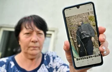 Olga Gavrilyuk, grandmother of Nazar Gavrilyuk, last June 21 holds up a photograph of the corpse of her son, Nazar's father, on her phone outside her home in Bucha, Ukraine, where Russian forces are accused of committing atrocities against civilians. [Sergei Supinsky/AFP]