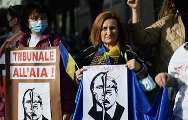 A woman holds a placard reading 'International Criminal Court in The Hague' above the portraits of both Russian President Vladimir Putin and Belarusian leader Alyaksandr Lukashenka during a pro-Ukrainian demonstration in front of Russia's embassy in Rome on February 24, 2022. [Filippo Monteforte/AFP]