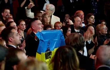 Ukrainian director Dmytro Sukholytkyy-Sobchuk holds an Ukrainian flag bearing the name of Maksym Butkevych, an Ukrainian human rights activist and journalist who is being held by Russia as a prisoner of war, during the 35th European Film Awards in Reykjavik, Iceland, on December 10, 2022. [Halldor Kolbenis/AFP]