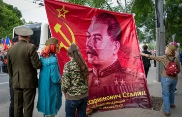 Moldovans stand near a flag with a portrait of Soviet dictator Joseph Stalin as they march in Chisinau to celebrate Victory Day May 9. [Elena Covalenco/AFP]