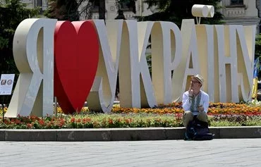 A man wearing a vyshyvanka, a traditional Ukrainian embroidered blouse, sits in front of a sign that says 'I love Ukraine' at Independence Square in Kyiv on June 18. [Sergei Supinsky/AFP]