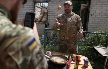 Ukrainian serviceman and influencer Ruslan Mokrytskyi cooks pasta as his fellow soldier records video of him for TikTok in an undisclosed location in Donetsk province on July 27. [Anatolii Stepanov/AFP]