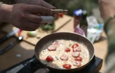 Ukrainian serviceman and influencer Ruslan Mokrytskyi shows a bullet casing containing spices while cooking pasta for a TikTok video in an undisclosed location in Donetsk province on July 27. [Anatolii Stepanov/AFP]