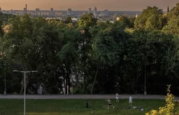 People play badminton in a park with the skyline of Kyiv in the background, on August 1, 2023, amid the Russian invasion of Ukraine. [Roman Pilipey/AFP]