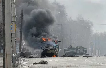 An unidentified soldier's body lies near a burning Russian armoured personnel carrier (APC) during fighting with the Ukrainian armed forces in Kharkiv, on February 27, 2022. [Sergey Bobok/AFP]