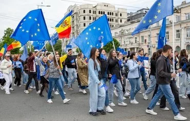 Young Moldovans waving EU and Moldovan flags march in Chisinau to celebrate Europe Day on May 9. [Elena Covalenco/AFP]