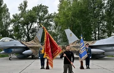 Ukrainian President Volodymyr Zelenskyy August 4 carries a flag in front of two F-16 fighter jets during a Ukrainian Air Force Day ceremony at an undisclosed location. [Sergei Supinsky/AFP]