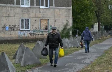 Местные жители проходят мимо расставленных на улице бетонных заграждений. Покровск, Донецкая область, 20 октября. [Женя Савилов/AFP]