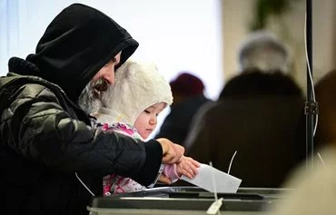 A Moldovan voter carries his child as he casts his vote for the presidential election in Chisinau November 3. [Daniel Mihailescu/AFP]