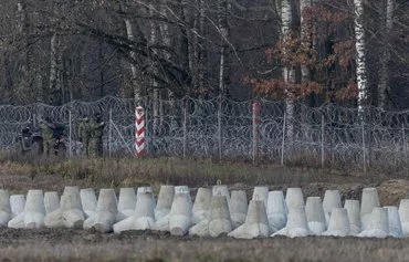 Border guards stand next to Polish and Russian border markings and concrete antitank barriers as Polish Prime Minister Donald Tusk inspects the first completed section of East Shield fortifications on the Polish-Russian border near Dąbrówka, Poland, on November 30. [Wojtek Radwanski/AFP]