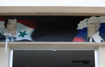 Defaced portraits of toppled Syrian dictator Bashar al-Assad and Russian President Vladimir Putin hang above an entrance to a building, reportedly used by the Russian army, in al-Bassah, Latakia province, Syria, December 12. [Aaref Watad/AFP]