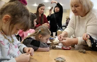 Татьяна Салиева (справа), директор театральной студии «Феликс» при Народном доме в Бахмуте, проводит мастер-класс по изготовлению рождественских украшений с членами бахмутской общины. Перед рождественским концертом, организованным бахмутской мэрией в изгнании. Киев, 23 декабря. [Анатолий Степанов/AFP]