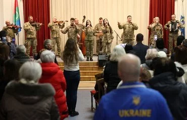 Внутренне перемещенные украинские граждане, члены бахмутской общины, слушают стоя Национальный Образцовый оркестр Вооруженных сил Украины на рождественском концерте, организованном мэрией Бахмута в Киеве, 23 декабря. [Анатолий Степанов/AFP] [Anatolii Stepanov/AFP]