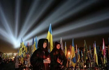 A symbolic illumination called "Rays of Memory" is seen over the graves of Ukrainian soldiers who died in the war with Russia, as people visit the Lychakiv Military Cemetery in Lviv on February 23, on the eve of the third anniversary of Russia's invasion of Ukraine. [Yuriy Dyachyshyn/AFP]