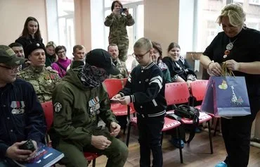 Schoolboy Ivan Ilyin, 7, presents a gift to Anatoly, a Russian veteran, during a ceremony led by local patriotic movements to reward Ivan for the drawings, messages and gifts he sent to Russian soldiers invading Ukraine, at a school in Istra, Moscow province, January 24. [Tatyana Makeyeva/AFP]